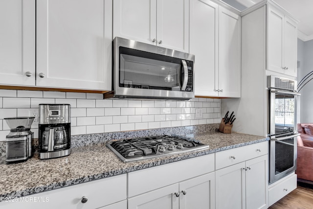 kitchen featuring light stone counters, stainless steel appliances, white cabinets, and decorative backsplash