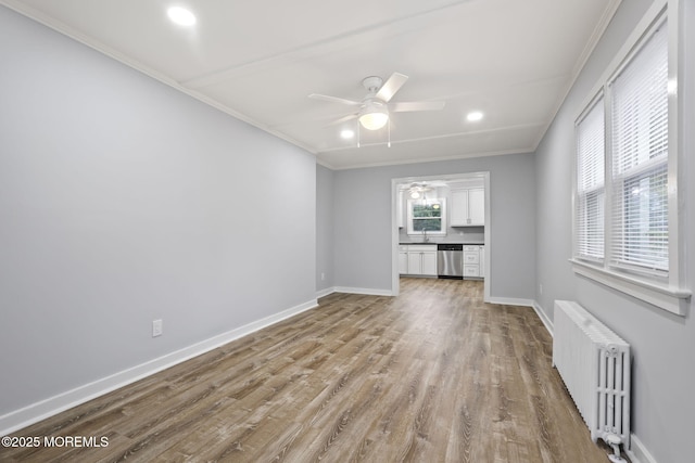 unfurnished living room with light wood-type flooring, crown molding, ceiling fan, radiator heating unit, and sink