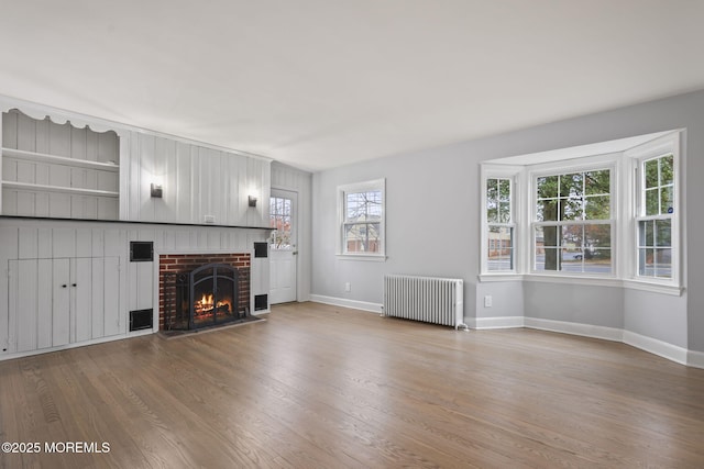 unfurnished living room featuring radiator, wood-type flooring, and a brick fireplace