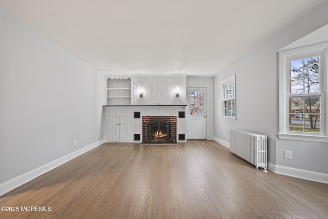 unfurnished living room featuring radiator, a brick fireplace, hardwood / wood-style floors, and a healthy amount of sunlight