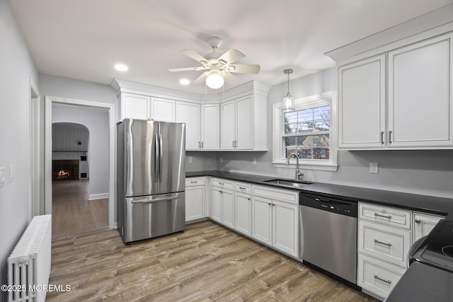 kitchen with stainless steel appliances, sink, hardwood / wood-style flooring, a brick fireplace, and radiator heating unit