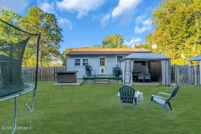 rear view of property featuring a gazebo, a yard, a jacuzzi, and a trampoline