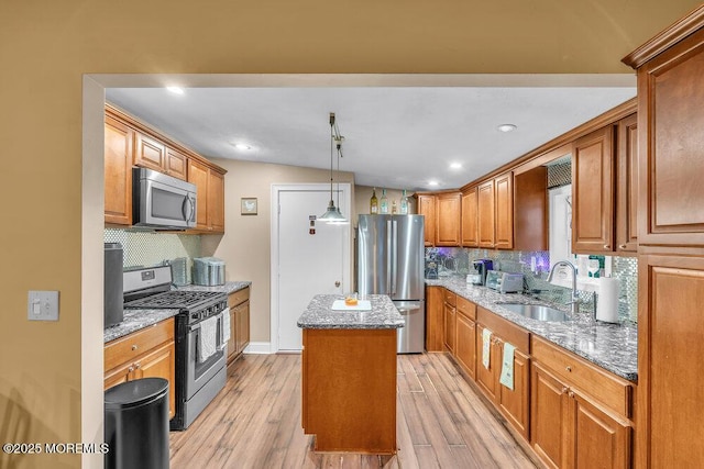 kitchen featuring appliances with stainless steel finishes, light stone counters, a kitchen island, sink, and light hardwood / wood-style flooring