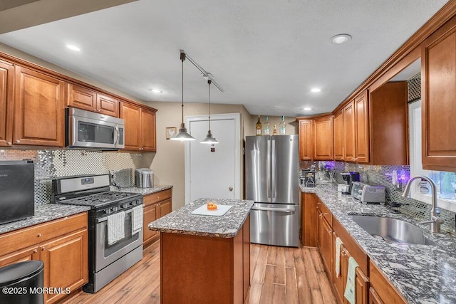 kitchen with light hardwood / wood-style floors, stainless steel appliances, a center island, sink, and stone countertops