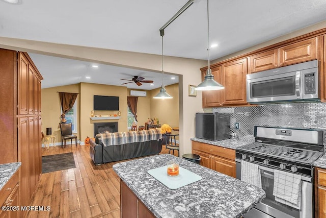 kitchen featuring tasteful backsplash, light stone countertops, a kitchen island, pendant lighting, and appliances with stainless steel finishes