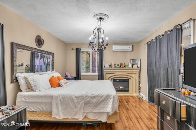 bedroom with a textured ceiling, an AC wall unit, a notable chandelier, and hardwood / wood-style flooring