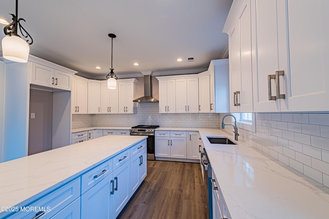 kitchen with decorative light fixtures, wall chimney range hood, sink, white cabinetry, and stainless steel appliances