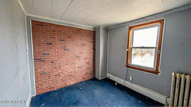 empty room featuring radiator, dark carpet, and brick wall