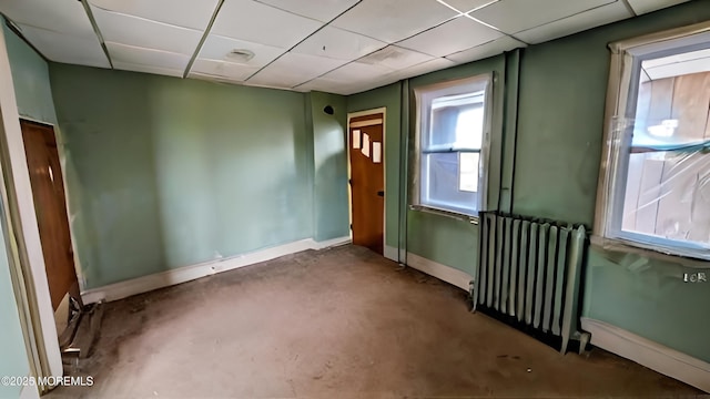 unfurnished room featuring radiator heating unit and a drop ceiling