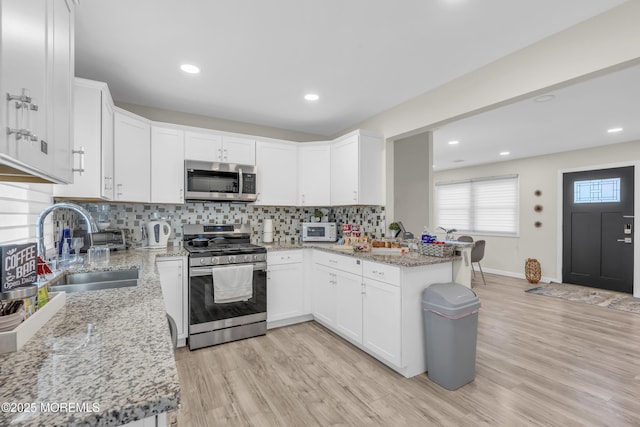 kitchen with light stone counters, appliances with stainless steel finishes, sink, and white cabinets