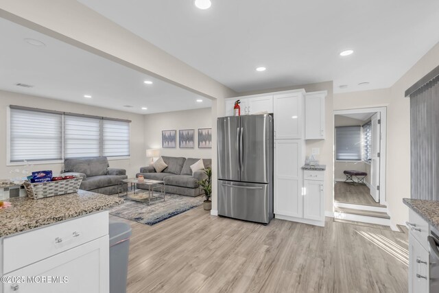 kitchen with stainless steel refrigerator, white cabinetry, light stone countertops, and light hardwood / wood-style flooring