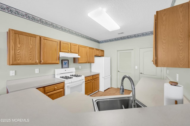 kitchen with white appliances, light wood-type flooring, a textured ceiling, and sink