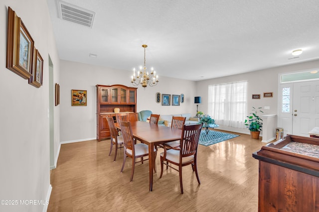 dining area with a textured ceiling, light hardwood / wood-style flooring, and an inviting chandelier