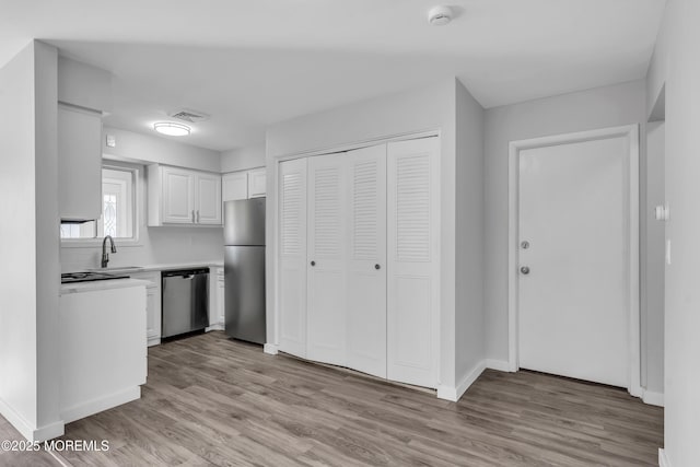 kitchen with light wood-type flooring, stainless steel appliances, white cabinets, and sink