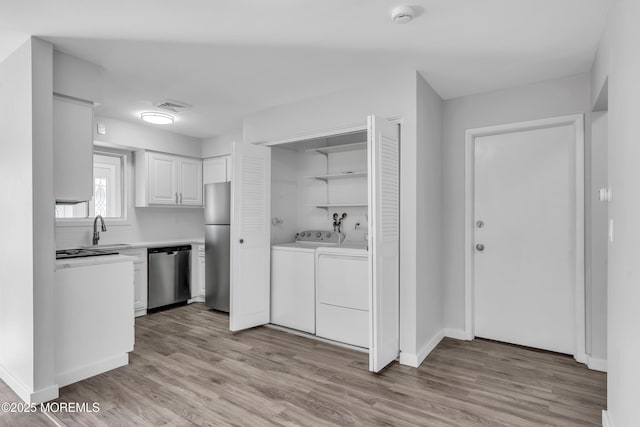 kitchen with white cabinets, appliances with stainless steel finishes, washing machine and clothes dryer, light hardwood / wood-style floors, and sink