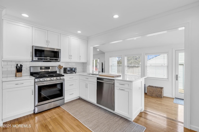 kitchen with appliances with stainless steel finishes, white cabinetry, backsplash, kitchen peninsula, and light hardwood / wood-style flooring