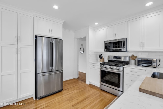 kitchen with appliances with stainless steel finishes, white cabinetry, decorative backsplash, light wood-type flooring, and light stone counters