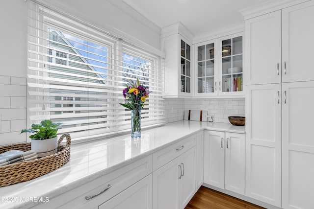 kitchen with light hardwood / wood-style floors, decorative backsplash, crown molding, white cabinetry, and light stone counters