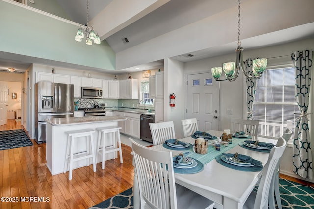 dining space with high vaulted ceiling, a notable chandelier, light hardwood / wood-style floors, and plenty of natural light