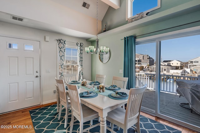 dining area with a chandelier, hardwood / wood-style floors, vaulted ceiling, and a water view