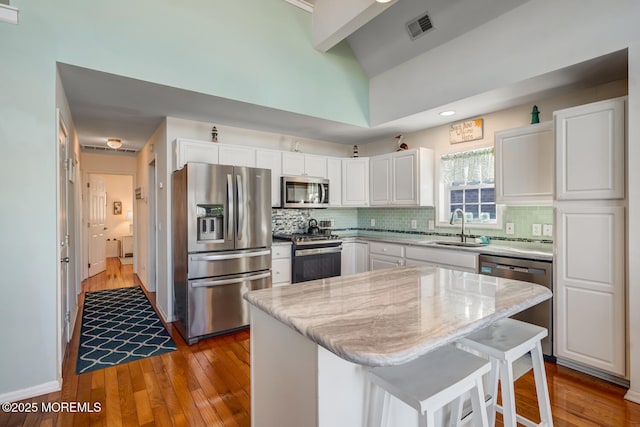 kitchen featuring appliances with stainless steel finishes, light stone counters, a kitchen island, sink, and white cabinetry