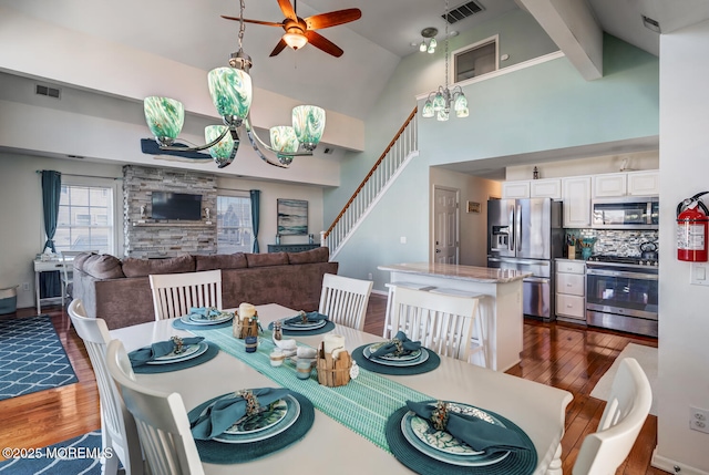 dining space with ceiling fan with notable chandelier, high vaulted ceiling, beamed ceiling, and dark hardwood / wood-style floors