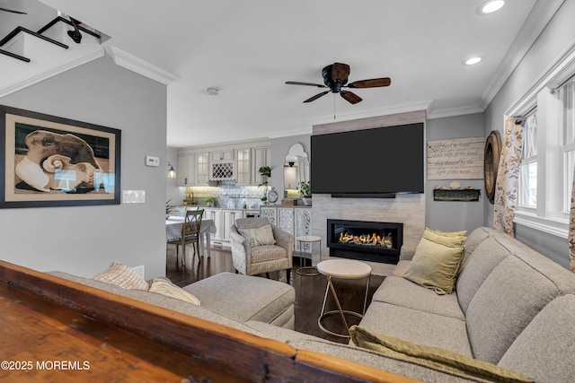 living room with ceiling fan, a tile fireplace, and ornamental molding