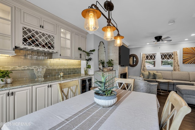 dining area with ceiling fan, dark wood-type flooring, ornamental molding, bar area, and beverage cooler