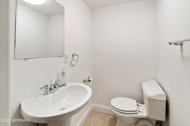 half bath with tile patterned flooring, baseboards, a sink, and toilet