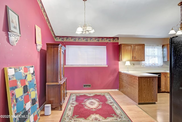 kitchen featuring black fridge, light hardwood / wood-style floors, kitchen peninsula, a chandelier, and pendant lighting