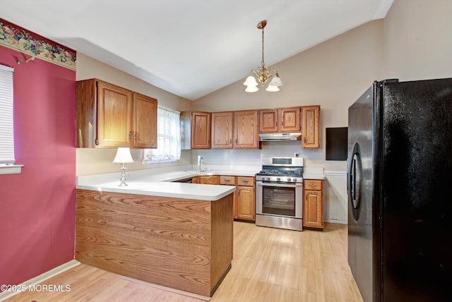 kitchen featuring an inviting chandelier, kitchen peninsula, stainless steel gas range oven, black fridge, and decorative light fixtures