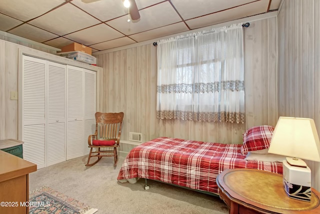 bedroom featuring wooden walls, carpet flooring, a drop ceiling, ceiling fan, and a closet