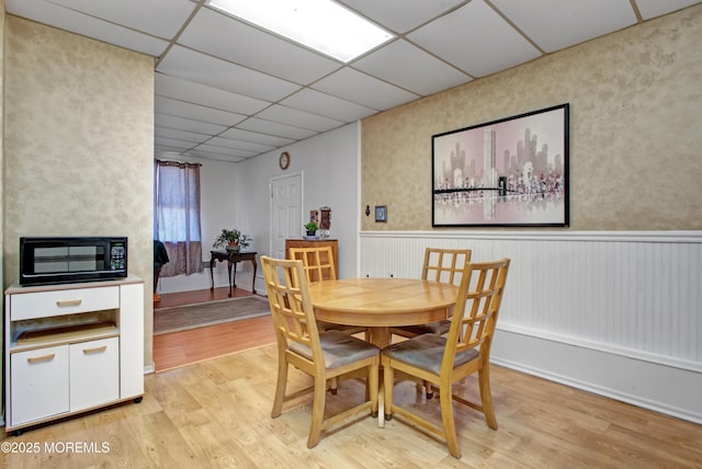 dining area with a paneled ceiling and light wood-type flooring