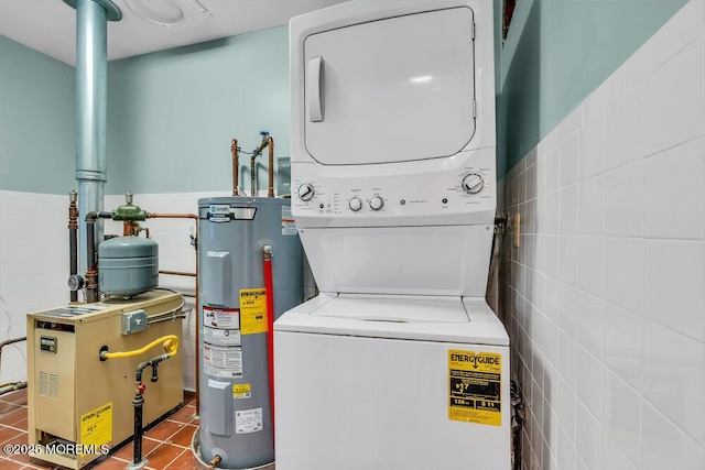 laundry area with stacked washer and dryer, tile patterned flooring, electric water heater, and tile walls