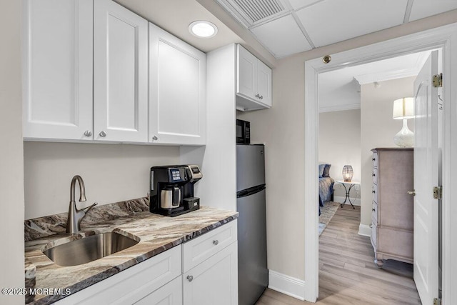 kitchen featuring white cabinets, stainless steel refrigerator, light hardwood / wood-style floors, light stone counters, and sink