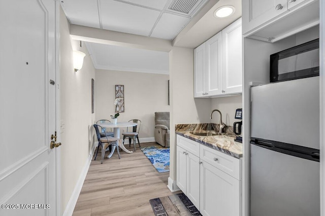 kitchen with sink, white cabinetry, stone counters, light hardwood / wood-style floors, and stainless steel refrigerator