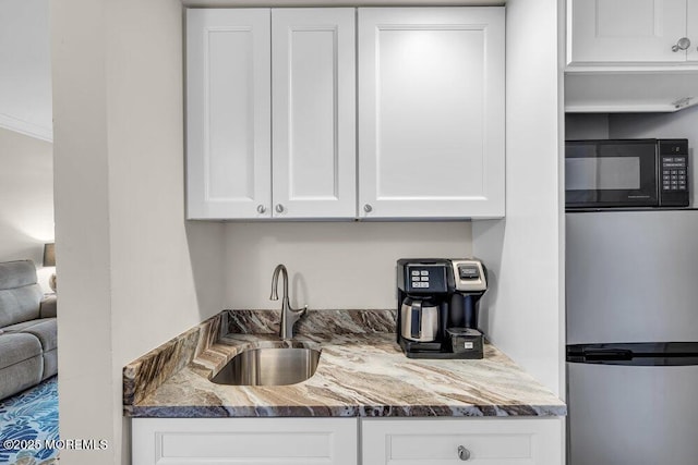 kitchen with white cabinets, stainless steel fridge, dark stone countertops, and sink