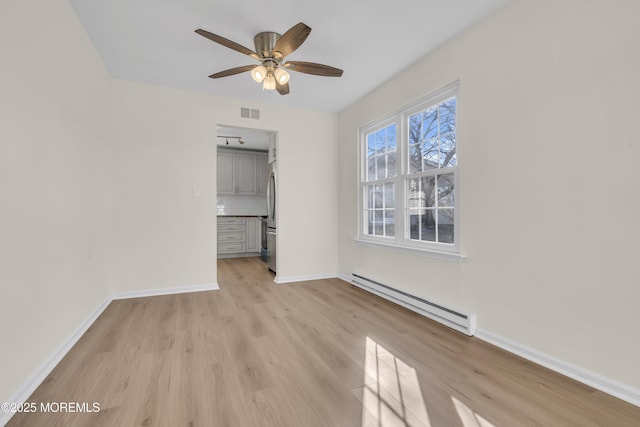 unfurnished bedroom with a baseboard radiator, a walk in closet, a closet, light wood-type flooring, and ceiling fan