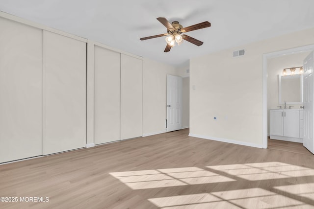 unfurnished bedroom featuring ensuite bathroom, ceiling fan, multiple closets, and light hardwood / wood-style flooring