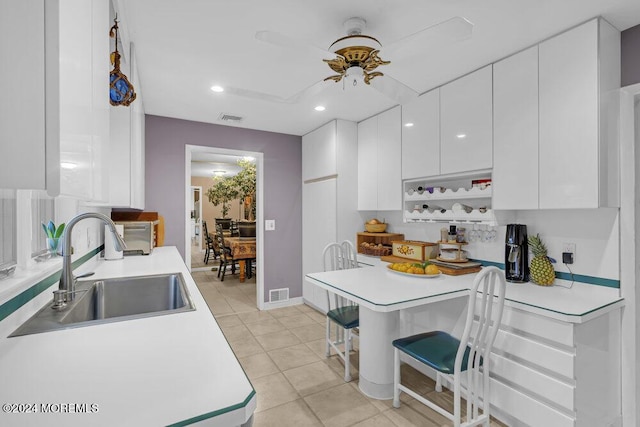 kitchen featuring light tile patterned floors, white cabinetry, a breakfast bar area, ceiling fan, and sink