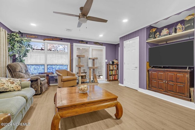 living room with ceiling fan, wooden walls, ornamental molding, and light wood-type flooring