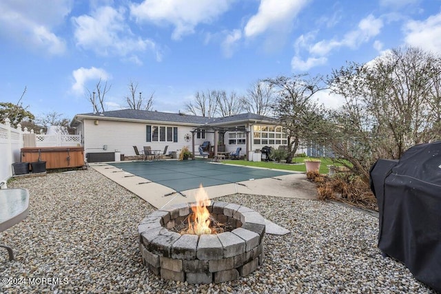 rear view of property featuring a fire pit, a sunroom, central AC unit, a hot tub, and a patio