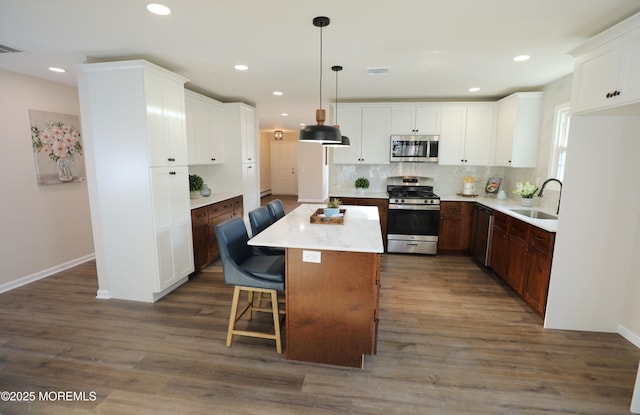 kitchen featuring dark wood-type flooring, a center island, appliances with stainless steel finishes, a kitchen breakfast bar, and sink