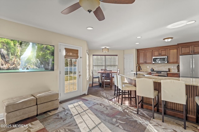 kitchen with stainless steel appliances, sink, ceiling fan, tasteful backsplash, and a breakfast bar area