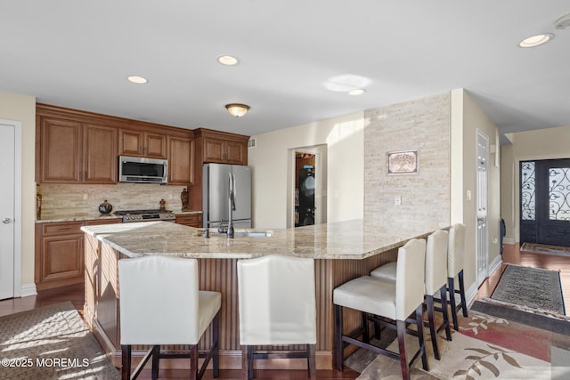 kitchen with kitchen peninsula, light stone countertops, stainless steel appliances, decorative backsplash, and a kitchen bar