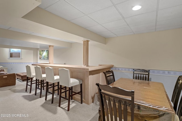 dining space featuring a paneled ceiling, bar area, and light colored carpet