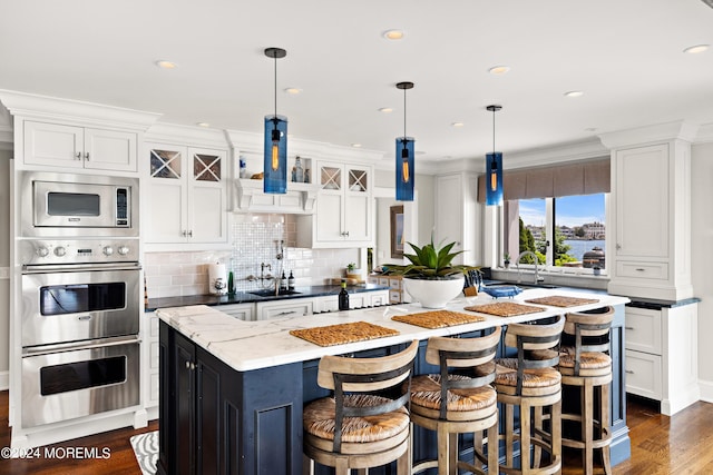 kitchen with decorative light fixtures, stainless steel appliances, a kitchen island, white cabinetry, and dark stone countertops