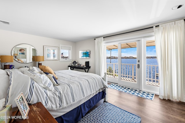 bedroom with dark hardwood / wood-style floors, access to exterior, and a water view