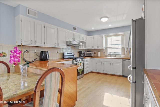 kitchen with stainless steel appliances, decorative backsplash, white cabinets, light hardwood / wood-style flooring, and sink