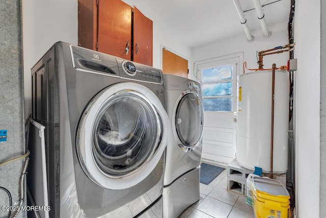 clothes washing area with washer and dryer, cabinets, gas water heater, and light tile patterned floors